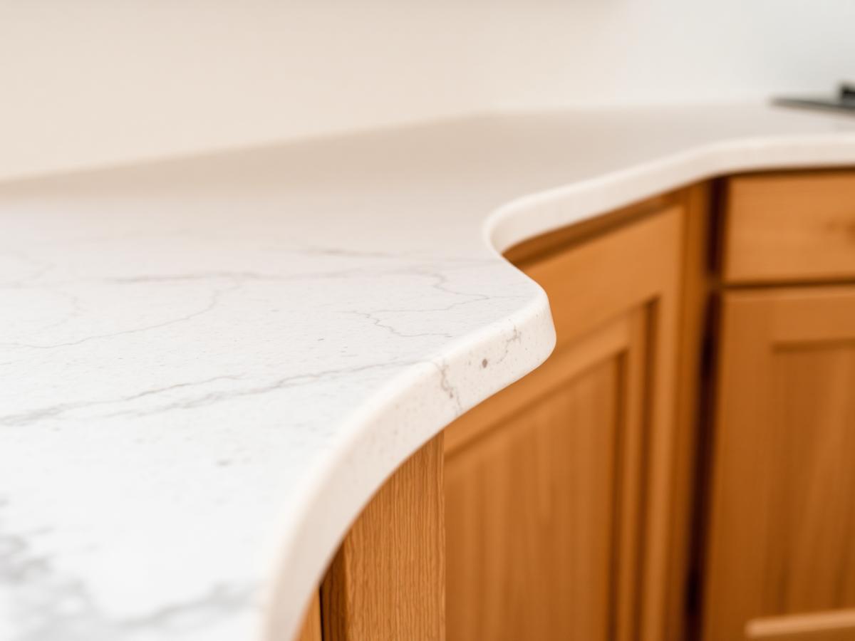 Conceptual close-up of a pale stone countertop edge above oak cabinetry